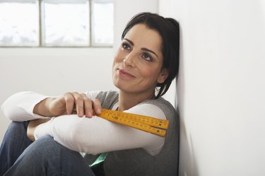 Woman leaning against wall holding measuring tape