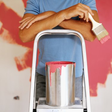 Close-up of a young man standing on a ladder with a paint bucket and brush